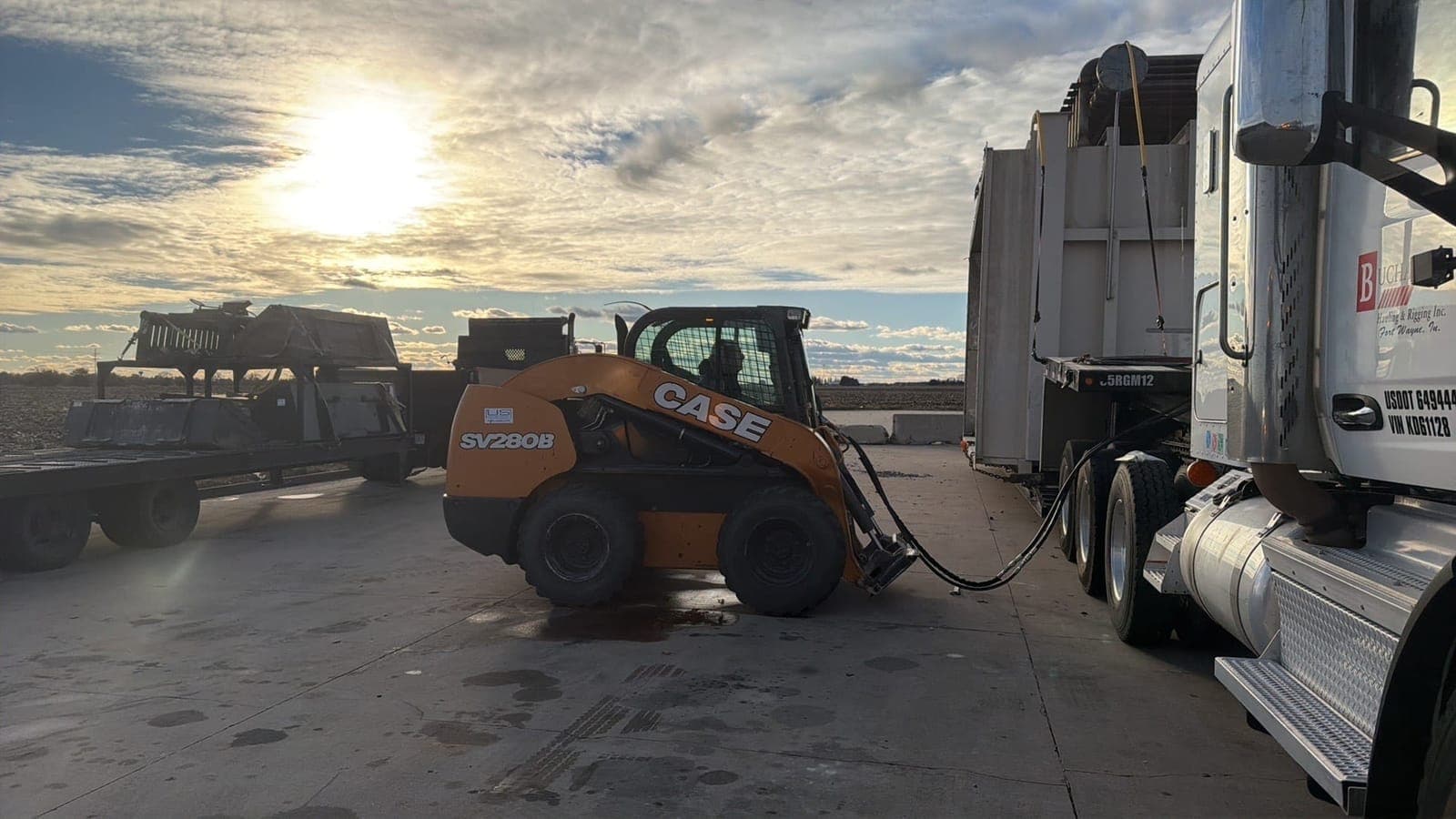 Skid steer loading trailer at sunset